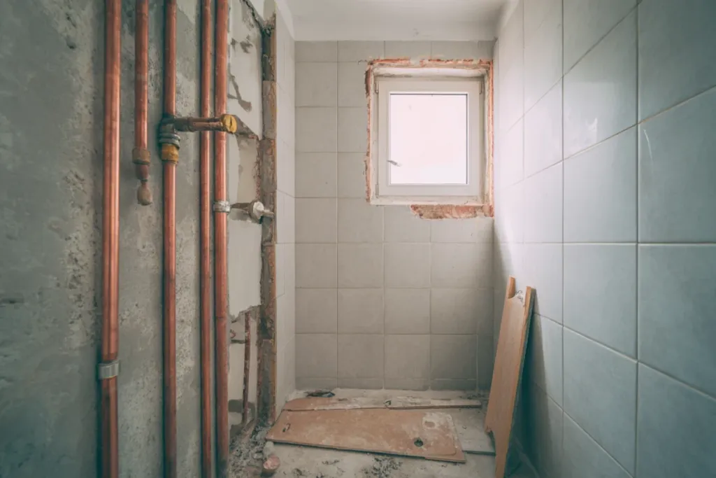 Baño a medio reformar con azulejos retirados y nuevas tuberías visibles